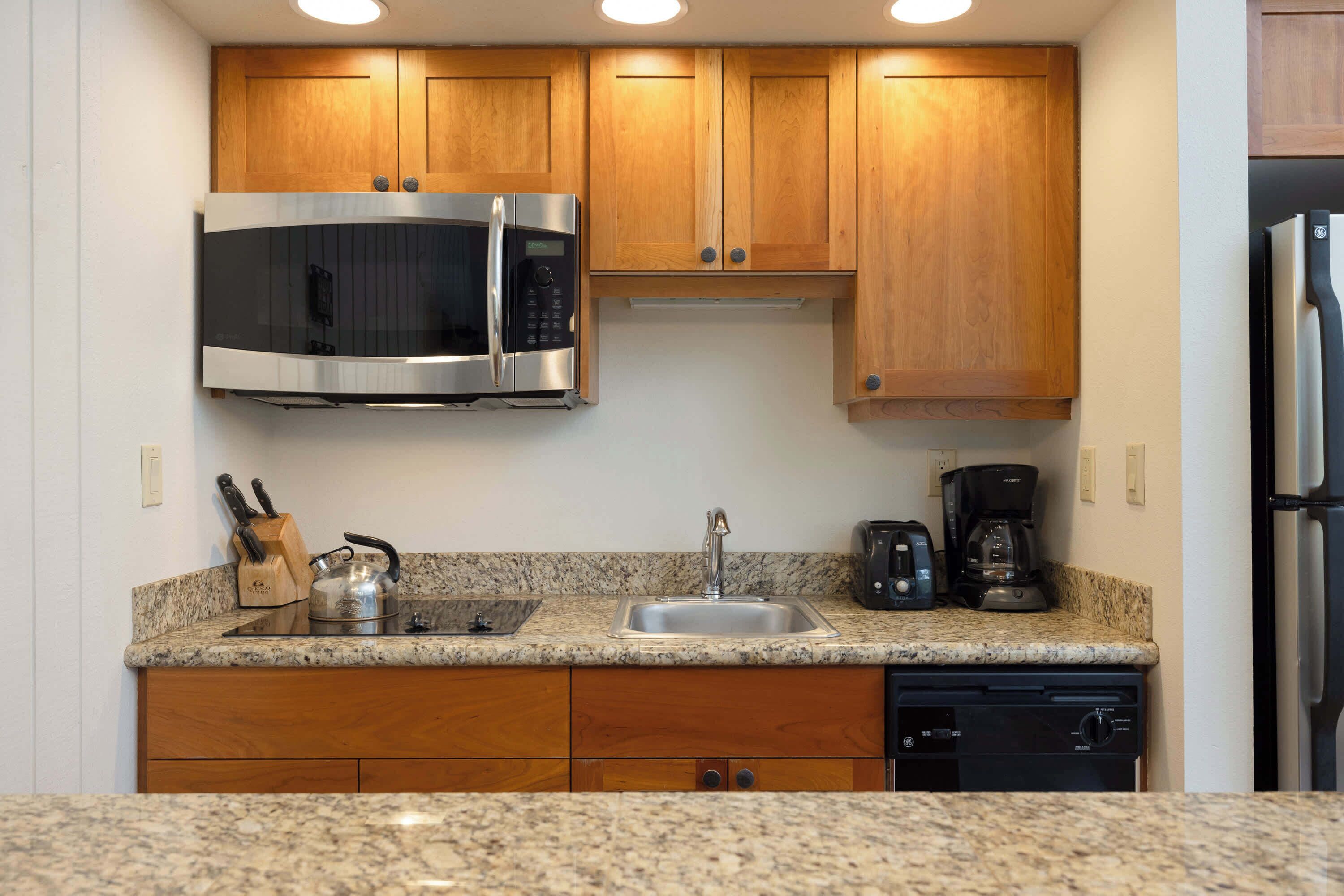A kitchen with wooden cabinets, a stainless steel microwave, a sink, a coffee maker, and a dishwasher.