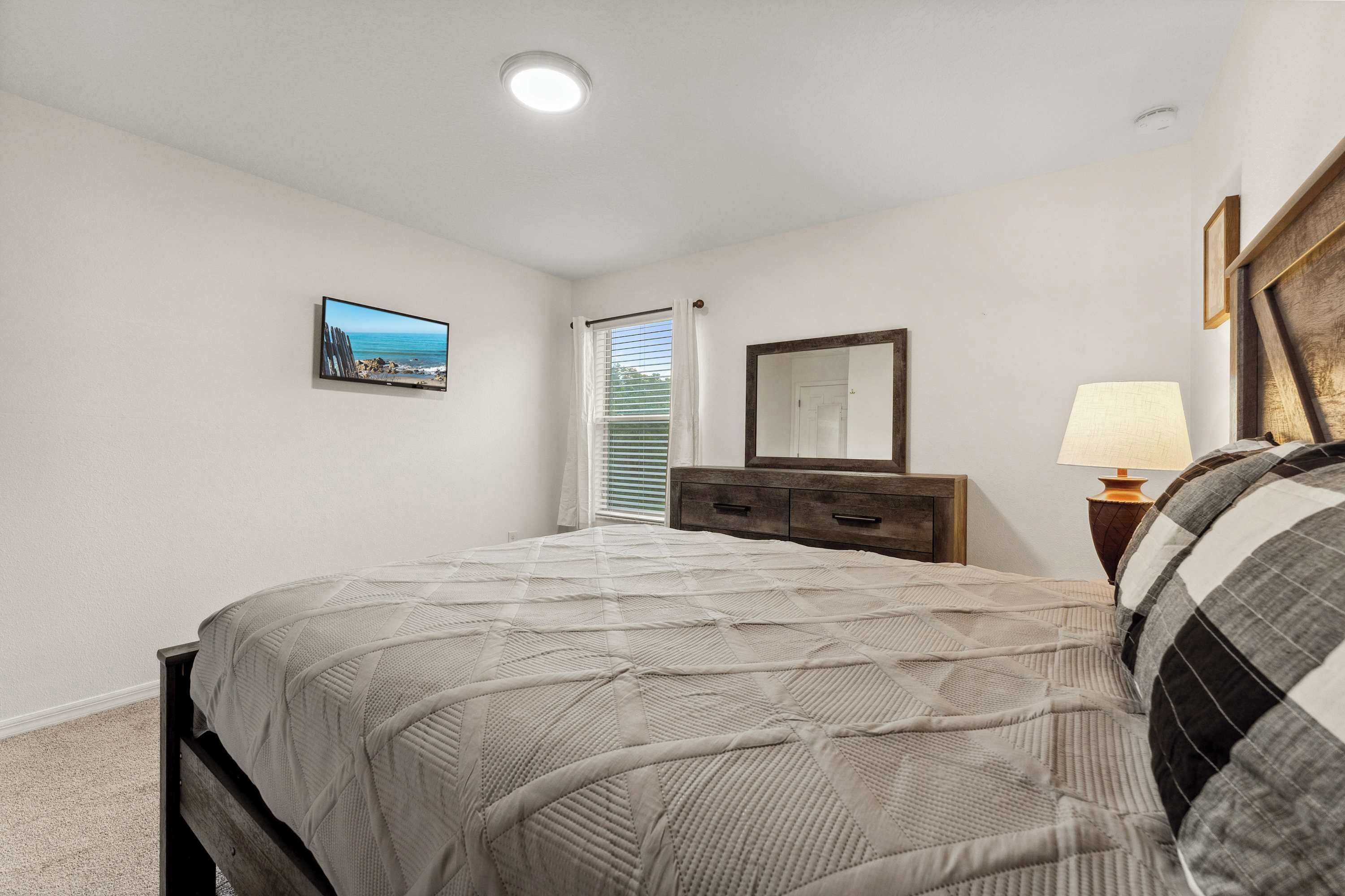 A bedroom with a bed, a dresser, a mirror, a lamp, and a picture on the wall.