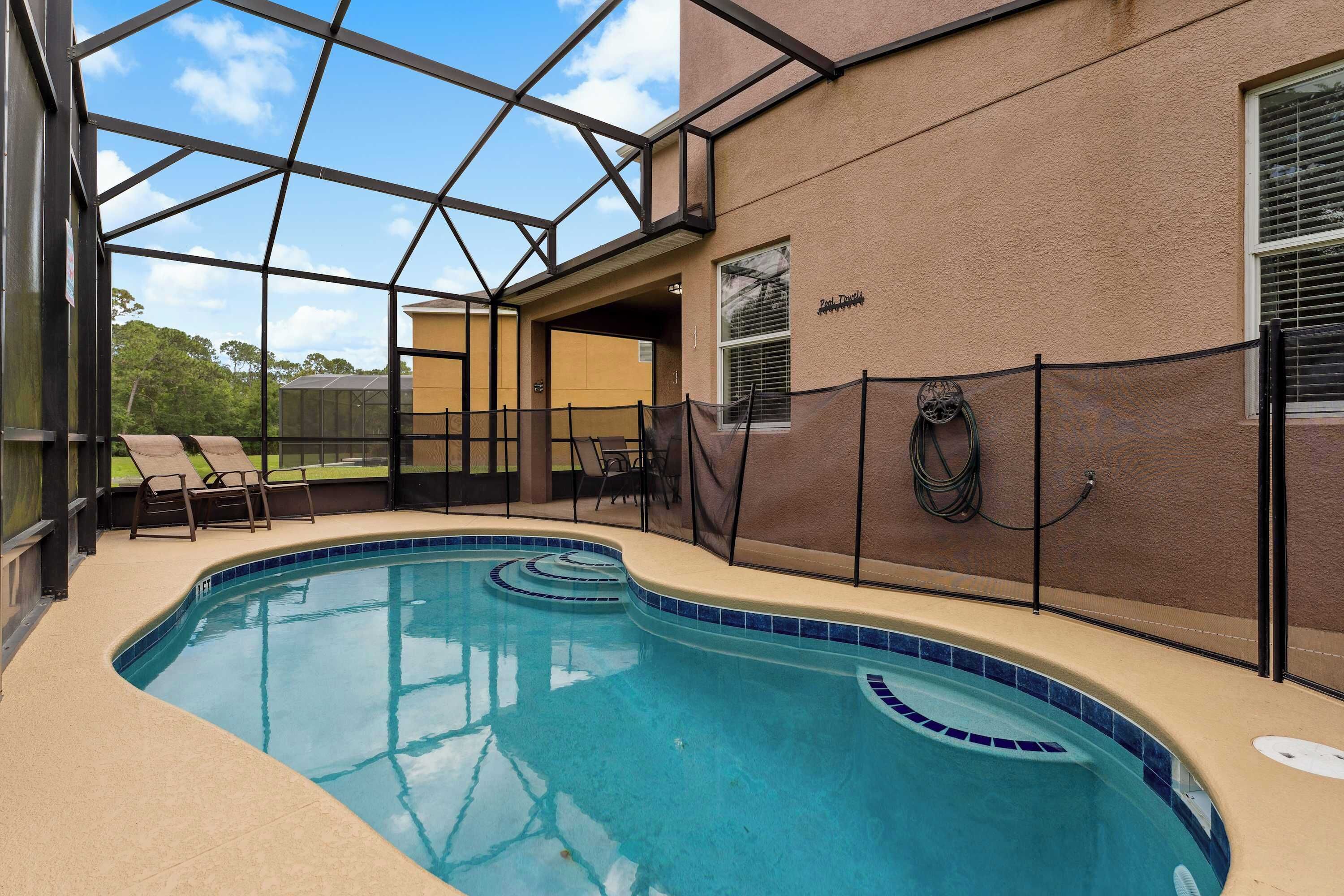 A swimming pool with a glass enclosure, lounge chairs, and a view of the surrounding area.