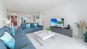 Ein modernes Wohnzimmer mit großem Flachbildfernseher, einem grauen Sofa, einem weißen Couchtisch und einem grauen Schrank.