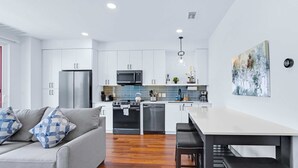 A modern kitchen with white cabinets, stainless steel appliances, and a dining area with a white table and black stools. - Chic Condo Minutes to Downtown, Gruene, & More (New Braunfels)