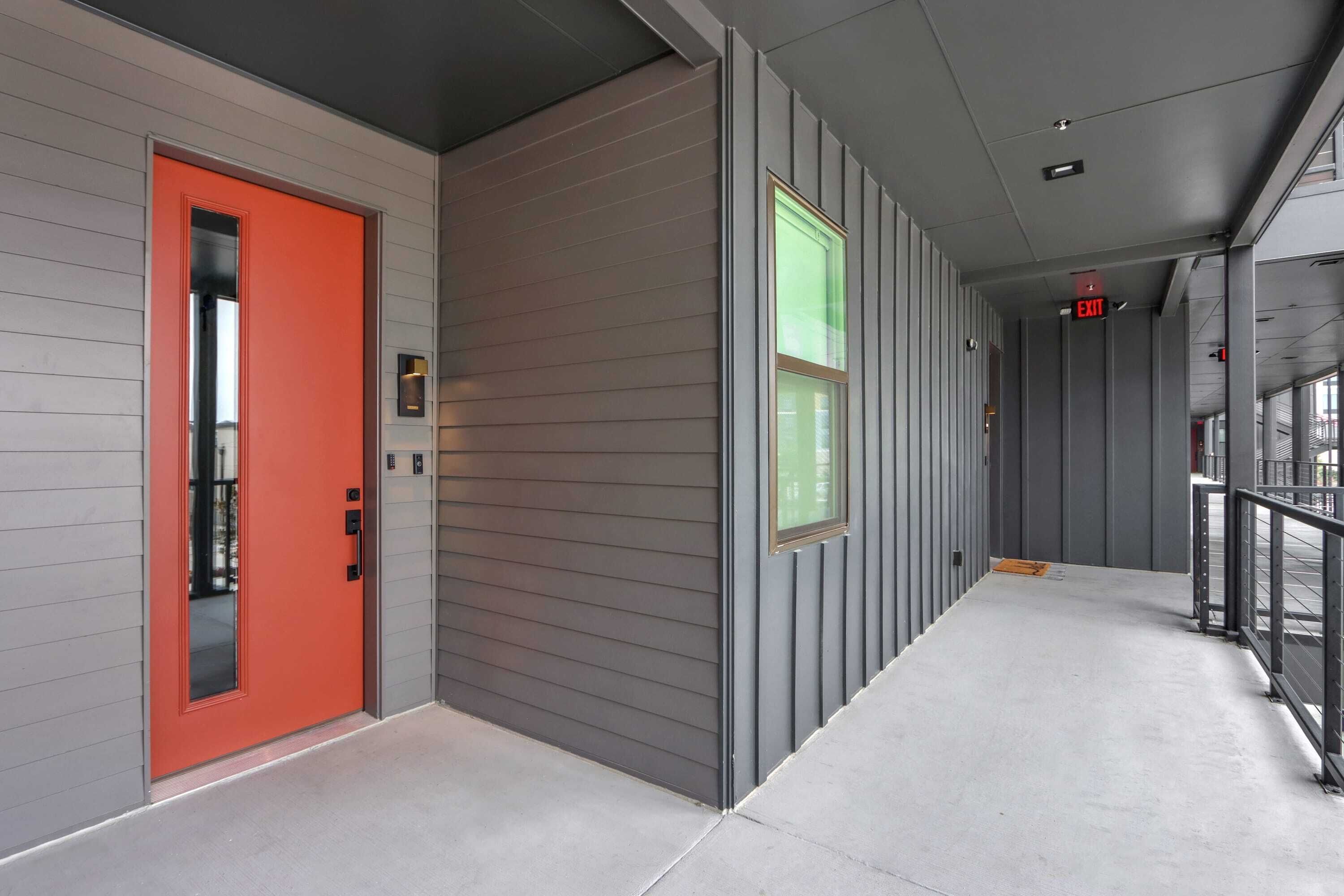 A hallway with a red door, a window, and an exit sign.