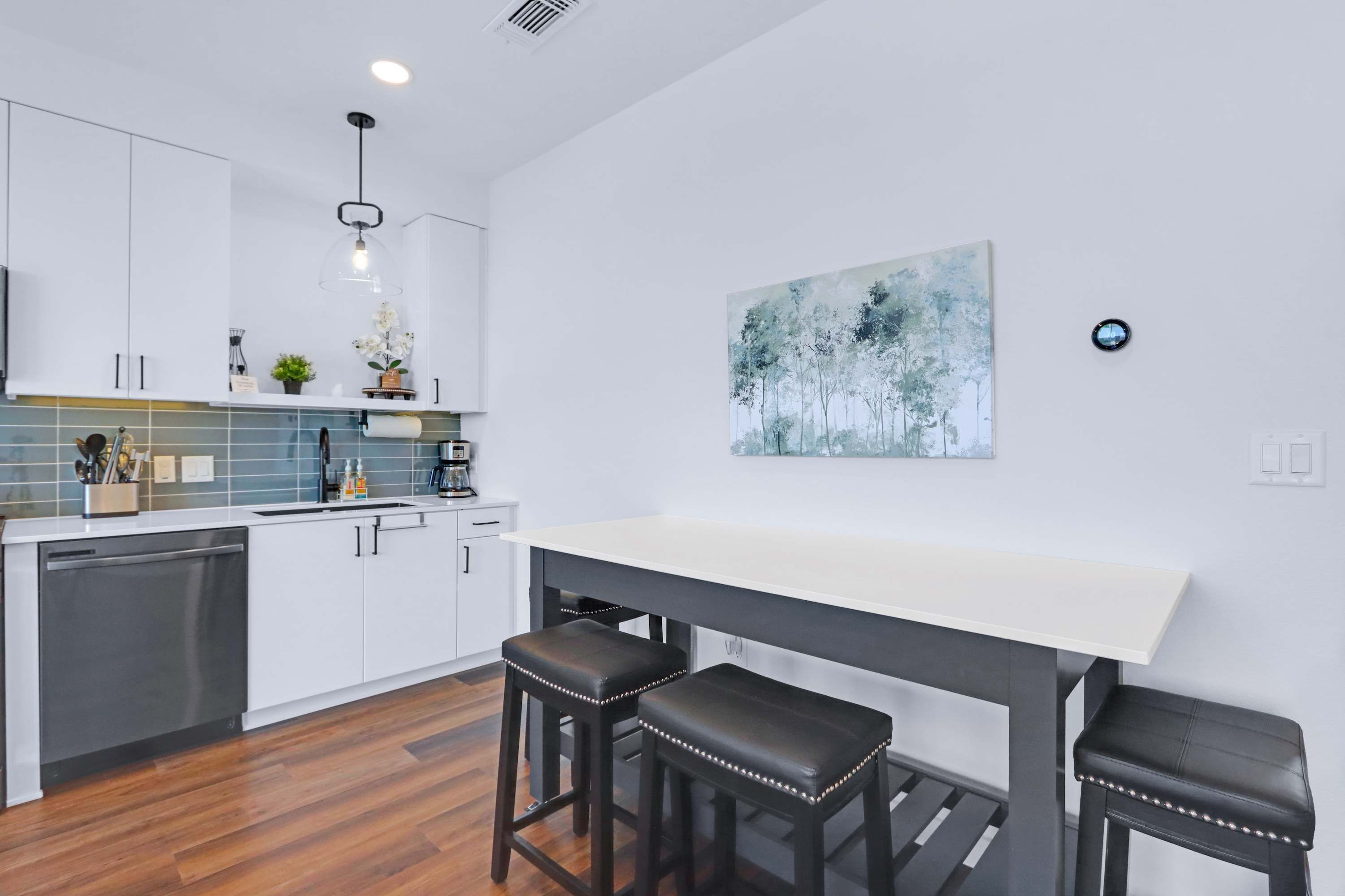 A modern kitchen with white cabinets, a black countertop, and a white dining table with three stools.