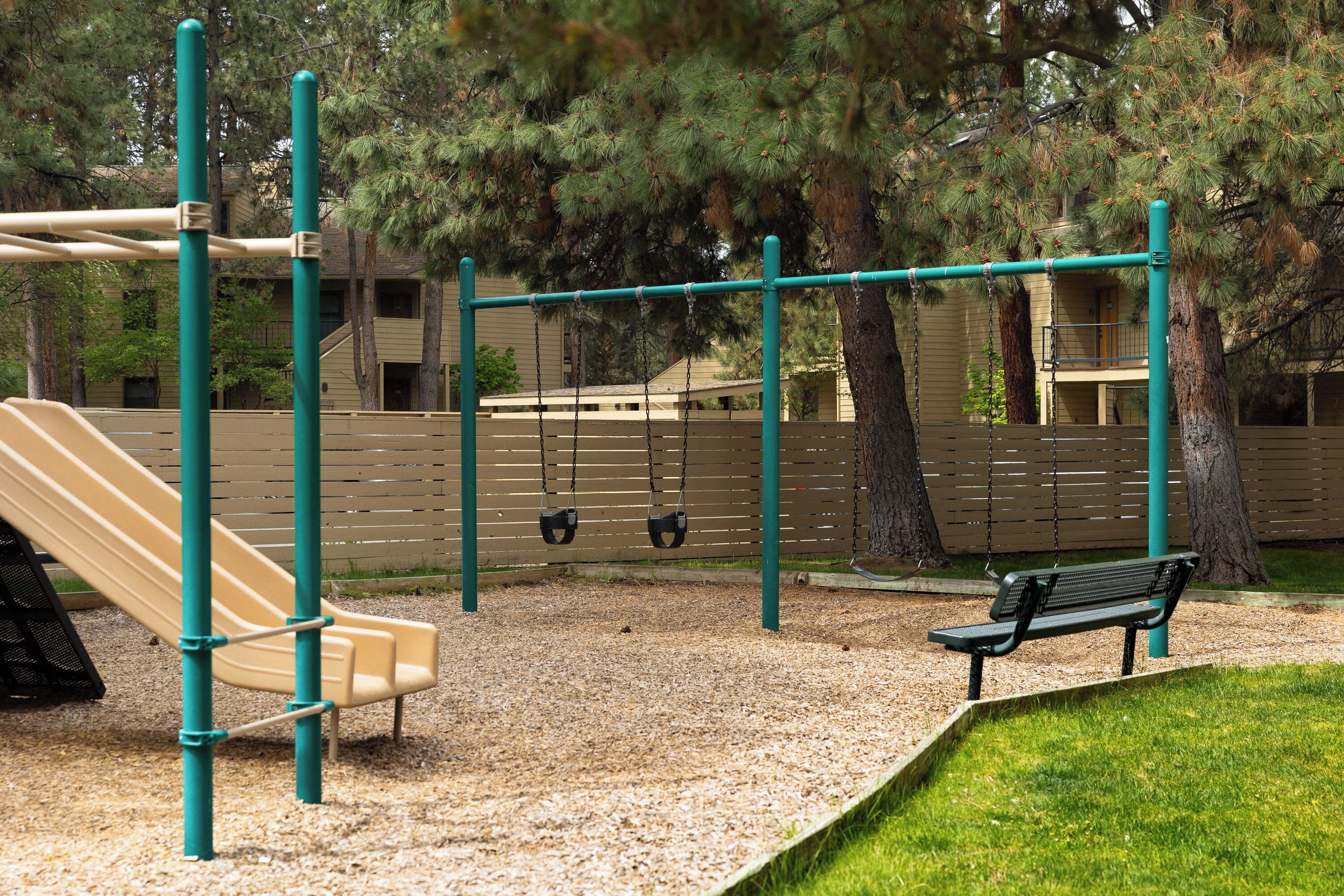 A playground with a slide, swings, and a bench.