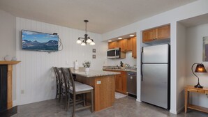 A modern kitchen with a central island, wooden cabinets, stainless steel appliances, and a mounted flat-screen TV. - Ponderosa Vista Resort Condo! (Bend)