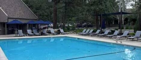 A swimming pool with lounge chairs and umbrellas, surrounded by trees.