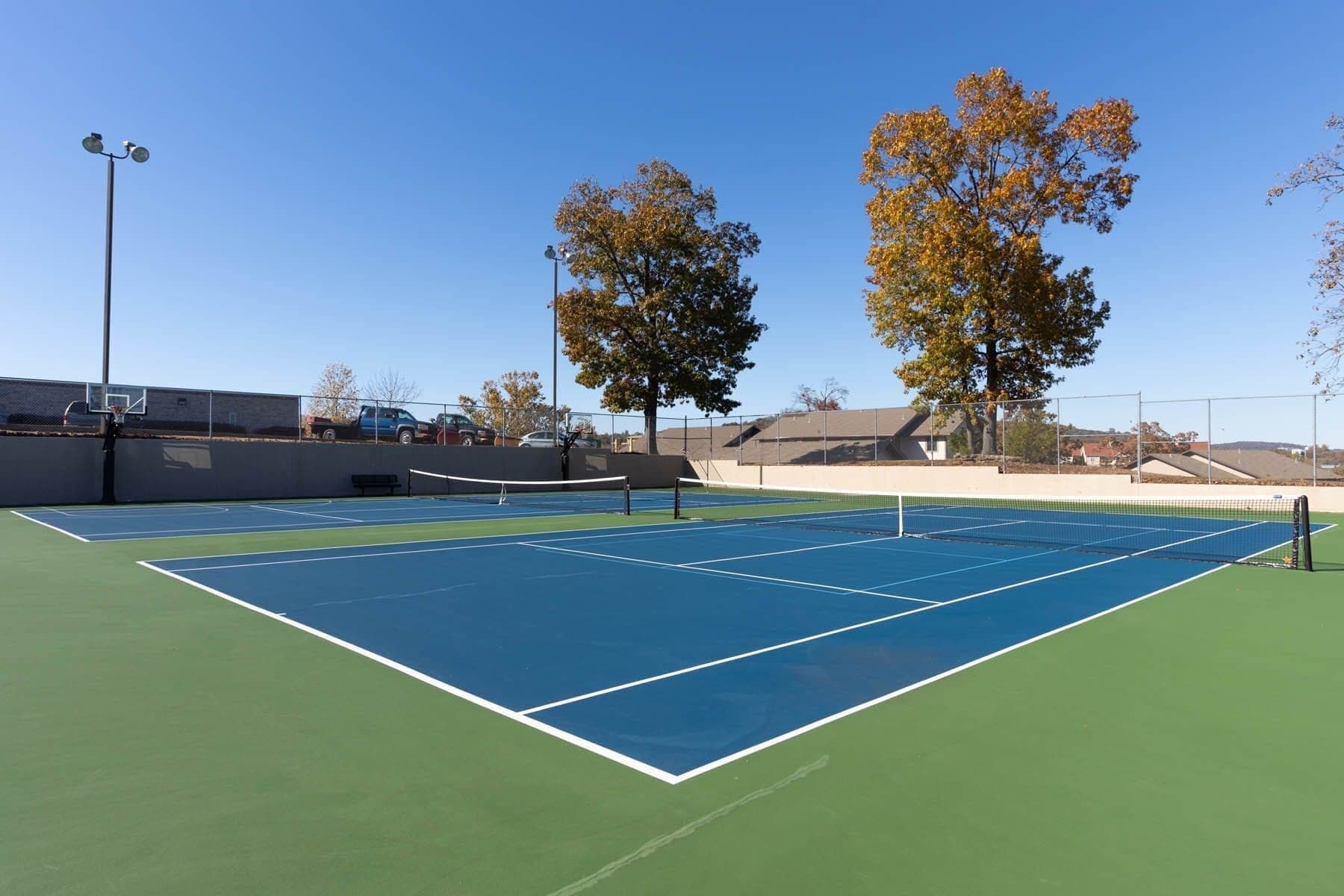 Una cancha de tenis exterior con red, rodeada de árboles y una valla.