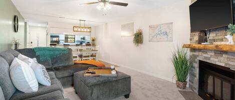 A living room with a sectional sofa, ottoman, fireplace, and ceiling fan.