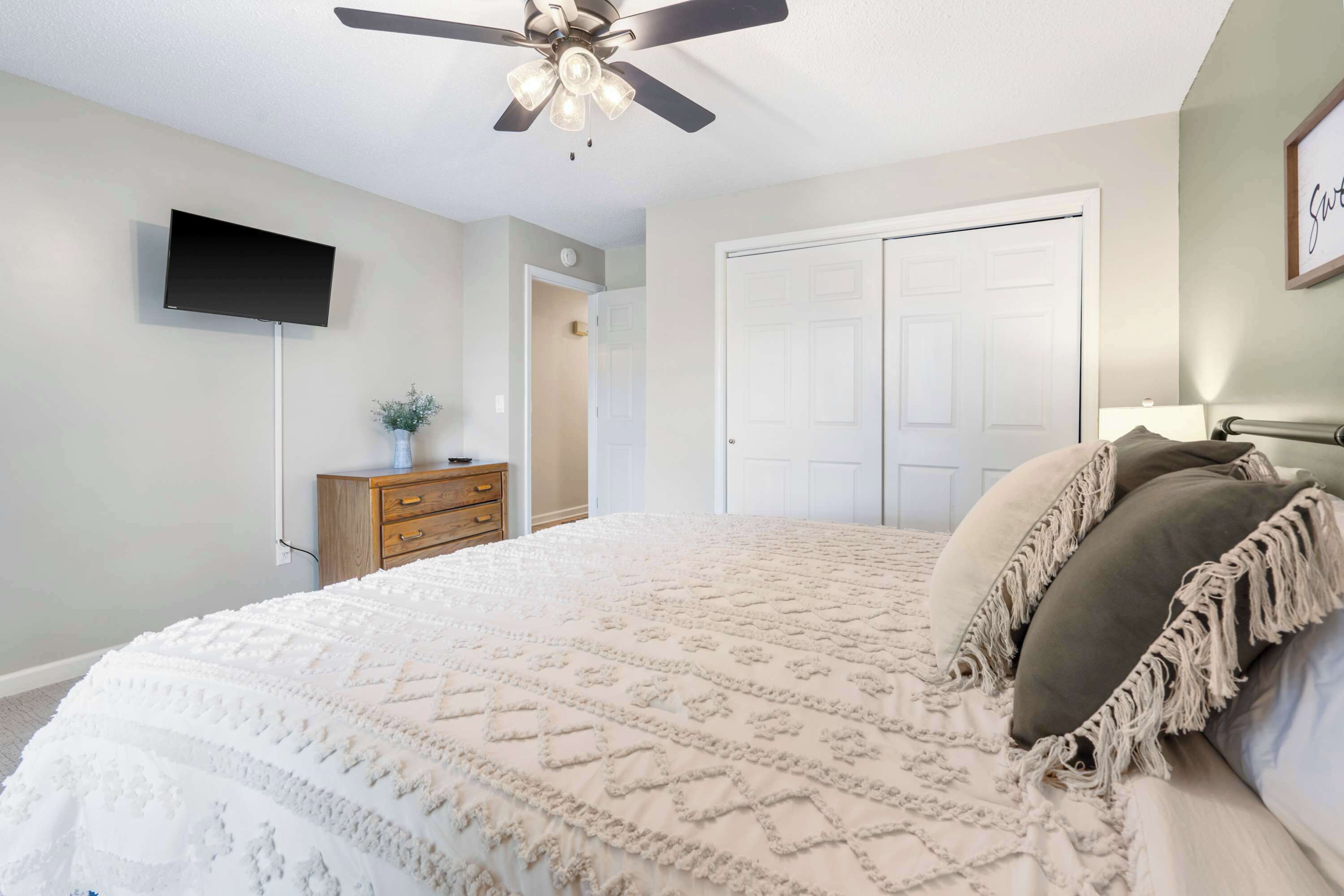 Un dormitorio con cama, ventilador de techo, televisor, cómoda y puerta.
