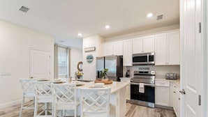 A modern kitchen with white cabinetry, stainless steel appliances, and a central island with bar stools. - Mint to Be (Kissimmee)