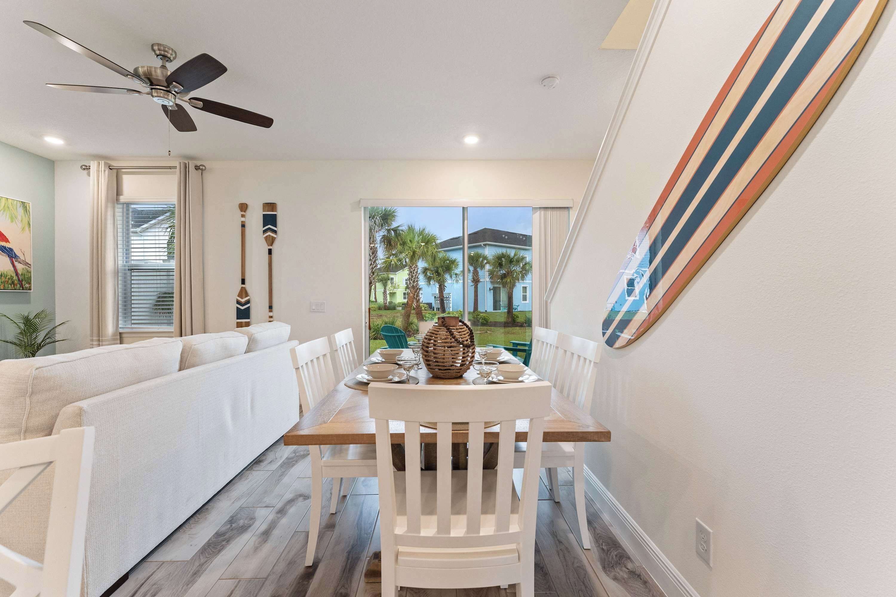 A dining area with a wooden table, white chairs, and a ceiling fan.