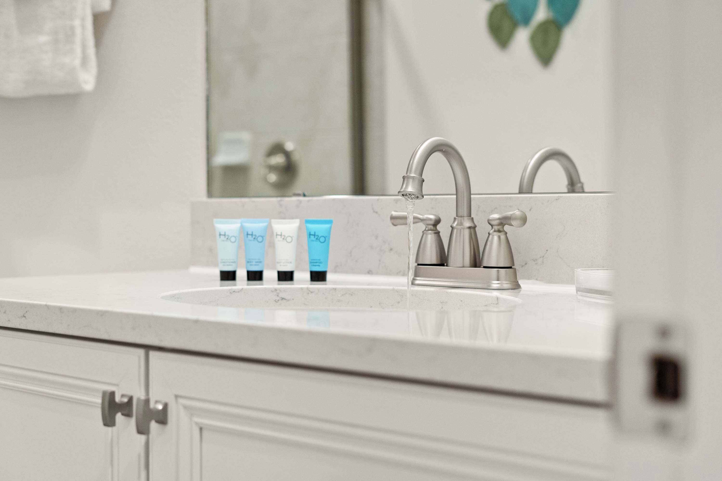 Un baño con encimera blanca, dos grifos y tres productos de higiene.