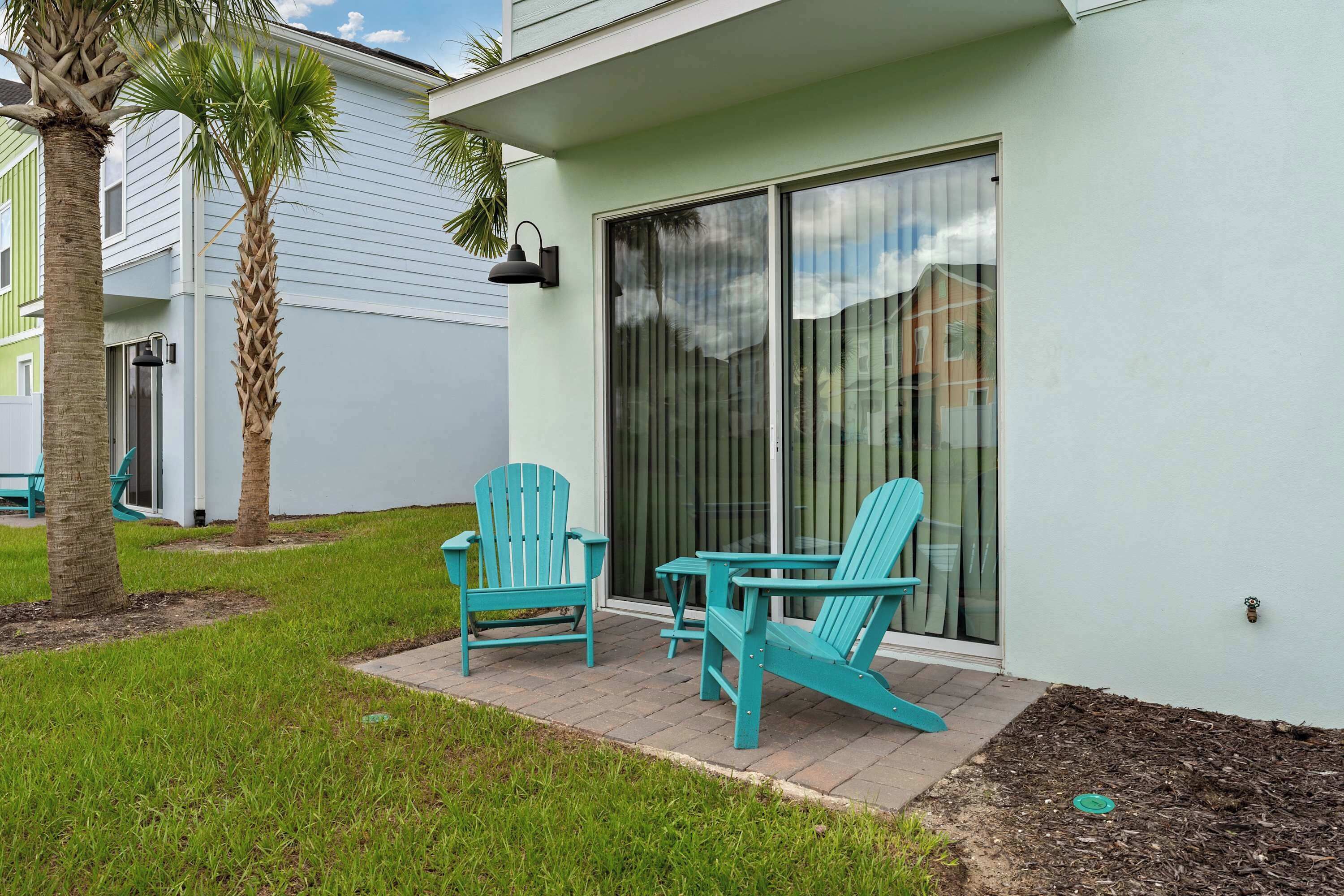A patio with two turquoise Adirondack chairs and a small table, a sliding glass door, and a palm tree.