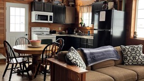 A cozy cabin interior with a wooden interior, a dining area with a round table and chairs, a sofa with patterned cushions, and a kitchen with modern appliances. - Welcome to The Fox Farm cabin  (Genoa)