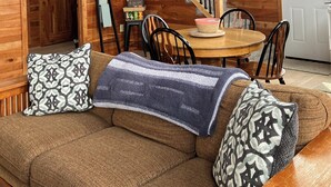 A wooden cabin interior with a staircase, a dining area, and a sofa with patterned cushions. - Welcome to The Fox Farm cabin  (Genoa)