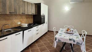 Una cocina compacta con gabinetes blancos, una encimera negra y una mesa de comedor con mantel blanco.