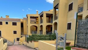 Una calle residencial con edificios amarillos, balcones y un muro de piedra con una reja.