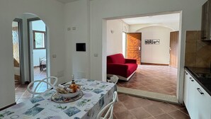 Un comedor con una mesa preparada para dos, un sofá rojo al fondo y una cocina visible a través de un umbral abierto.