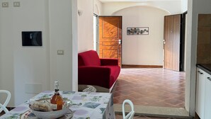 Un comedor con una mesa dispuesta para dos personas, un sofá rojo, y una cocina visible a través de un arco.