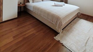 Un dormitorio con cama, armario, una mesita con una planta y ventana con cortinas.