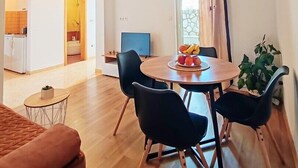 Un salón moderno con una mesa redonda de madera, sillas negras y una mesita auxiliar con una planta.
