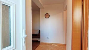 Un pasillo con una puerta de madera, un reloj en la pared y suelo de baldosas.