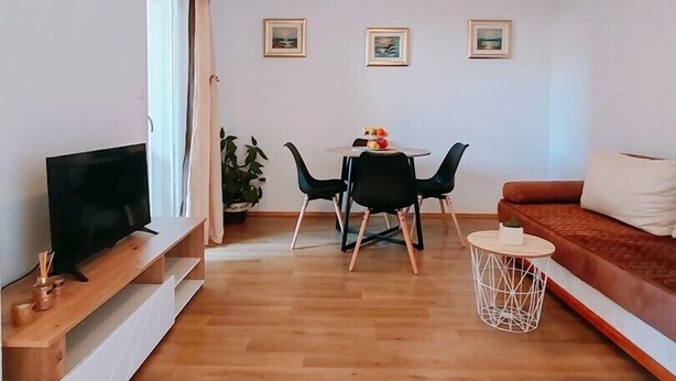 Una sala de estar moderna con un televisor de pantalla plana, una mesa de comedor con sillas, un sofá y una pequeña mesita auxiliar.