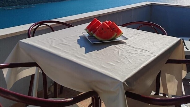 A balcony with a table and chairs, overlooking a body of water and distant hills.