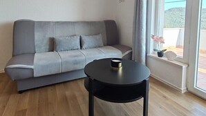 A modern living room with a grey sofa, a black coffee table, and a large window with a view of the outdoors.