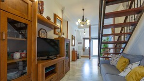 A living room with a television on a wooden stand, a sofa with cushions, and a staircase leading to another level. - Marina Beach in Fuengirola (Fuengirola)