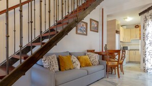 A living room with a grey sofa, wooden dining table, and chairs. A staircase with metal railings leads to an upper floor. - Marina Beach in Fuengirola (Fuengirola)