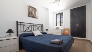 A bedroom with a bed, two bedside tables, a nightstand, a ceiling fan, a window with blinds, a door, and a wall-mounted artwork. - La Galera in Torredembarra (Torredembarra)
