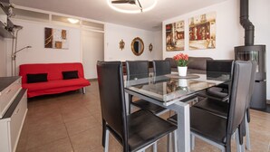 A modern dining area with a glass table and black chairs, a red sofa, and a black stove. - La Galera in Torredembarra (Torredembarra)