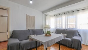A living room with a grey sofa, a small table with a plant, and a window with curtains. - Mirador De Triana in Sevilla (Seville)