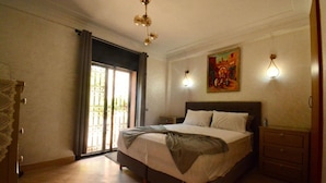 Une chambre à coucher avec un lit, une table de chevet, une commode, un tableau et une fenêtre avec des rideaux.
