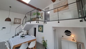 Un interior moderno con comedor, escalera y un altillo con barandilla de vidrio.