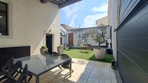 Un patio con mesa y sillas de vidrio, un pequeño césped y un árbol en maceta.