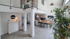 Una cocina moderna con una isla central, un comedor con sillas y una escalera que sube a un nivel superior.