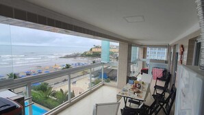 A balcony with a view of the beach and ocean, a dining area with a table and chairs, and a kitchen area with a stove and sink.