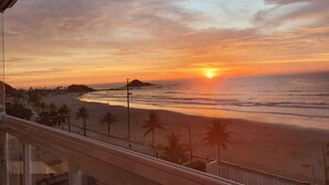 A sunset view from a balcony overlooking a beach with palm trees and a distant island.