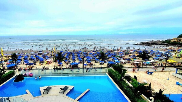 A beach resort with a large pool, numerous umbrellas, and a view of the ocean.