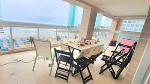 A balcony with a view of the beach, a table with chairs, and a bar area.