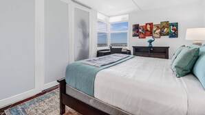 A bedroom with a large bed, a nightstand, a dresser, and a window with a view. - Estero Beach & Tennis 1206 A (Fort Myers Beach)