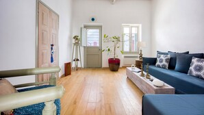 Ein Zimmer mit Holzboden, einem blauen Sofa, einer Holzbank, einem Blumentopf und einer Tür mit Fenster.