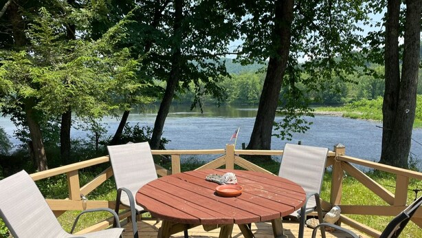 Eine Holzterrasse mit einem runden Tisch und vier Stühlen, mit Blick auf einen See.