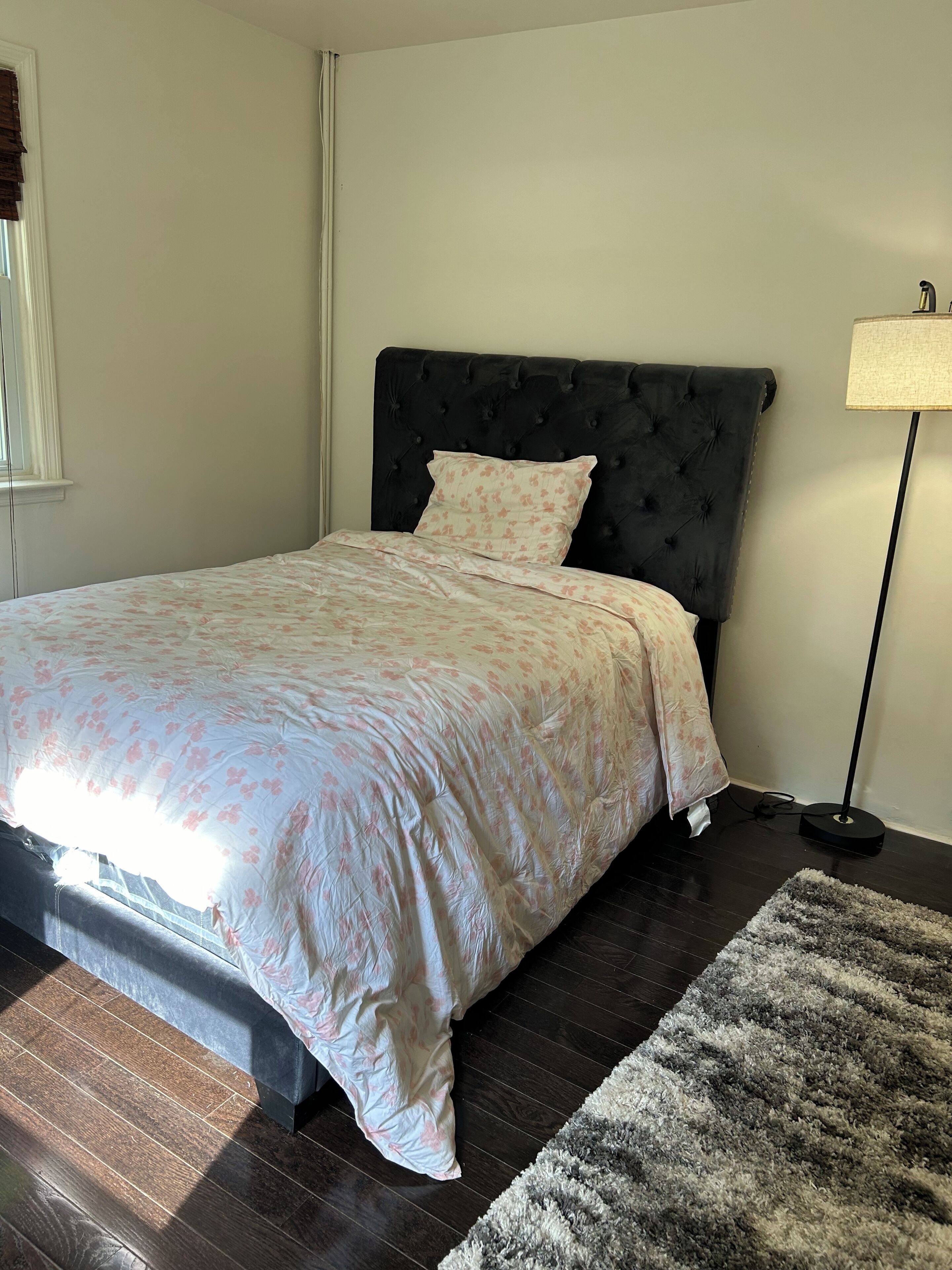 A bedroom with a bed, a dark headboard, a floor lamp, and a rug.