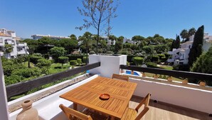 Une table et des chaises en bois sur un balcon donnant sur un quartier résidentiel.
