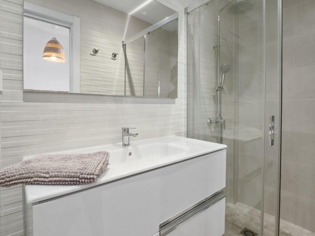 A modern bathroom with a white sink, a glass shower enclosure, and a large mirror above the sink.