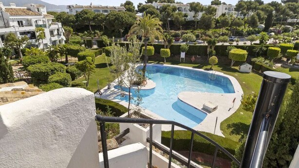 Une piscine au design incurvé, entourée de pelouses et d’arbres bien entretenus.