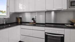 Une cuisine moderne avec des armoires blanches, un plan de travail noir, un four encastré et un four à micro-ondes.